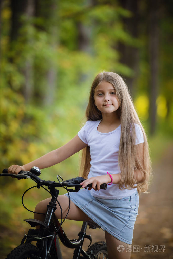 可爱的小女孩在阳光明媚的公园里骑自行车