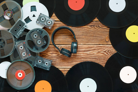 古老的老式线轴，乙烯基唱片，录音带和耳机放在木制桌子的背景上。五颜六色的标签。俯视图。复制空间的位置。