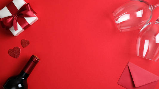 情人节相框。平放白色礼盒，红丝带蝴蝶结，一瓶香槟酒，两个玻璃杯和红色背景信封。情人节庆祝，浪漫晚餐情侣概念