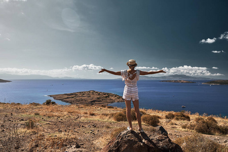 年轻的女旅行家，站在岩石上，举起双臂