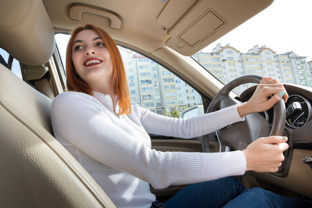 Young redhead woman driver behind a wheel driving a car smiling 