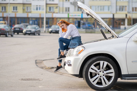 一位年轻的女司机在破车附近,引擎盖被炸开了照片