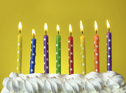 彩色蜡烛在黄色背景的生日蛋糕上燃烧