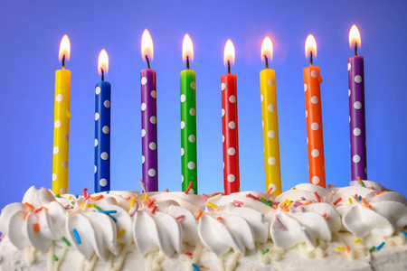 在蓝色背景的生日蛋糕上点上五颜六色的蜡烛