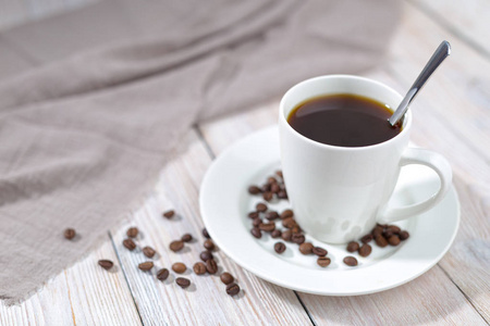 把一杯热咖啡和烤咖啡豆放在白色的木桌上。