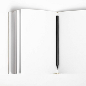 在白色纹理纸背景下的封闭空白方形书和黑色铅笔的模型