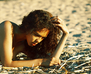 年轻漂亮的非洲卷发女孩在日落的海滩上看着，生活方式让人有概念