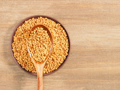 Fenugreek in clay plate and spoon on a brown wooden background. 