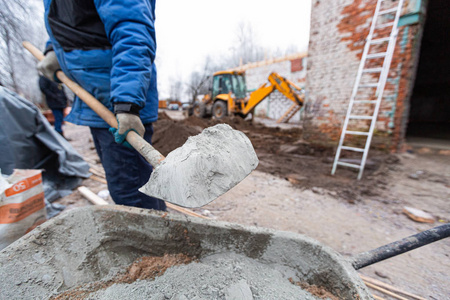施工现场戴防护手套的工人正在用铁锹将水泥装载到装有沙子的建筑台车