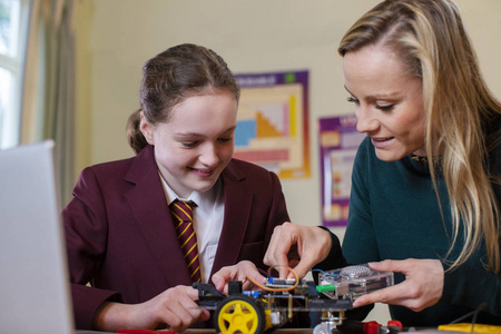 Teacher Helping Female Pupil Wearing Uniform To Build Robot Car 