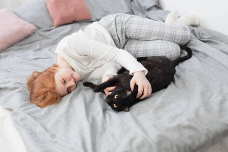 beautiful teenager girl with black cat on bed at home 