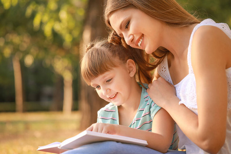 美丽的年轻女子和她的小女儿在公园里看书