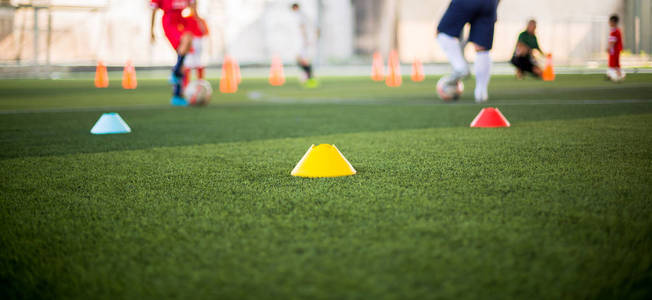 绿色人造草坪上的标志锥与模糊的儿童足球比赛