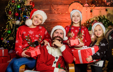 节日快乐。父亲留着大胡子的男人，母亲的背景是可爱的女儿圣诞树。花时间和你的家人在一起。家长和孩子们打开圣诞礼物。圣诞节的传统。节