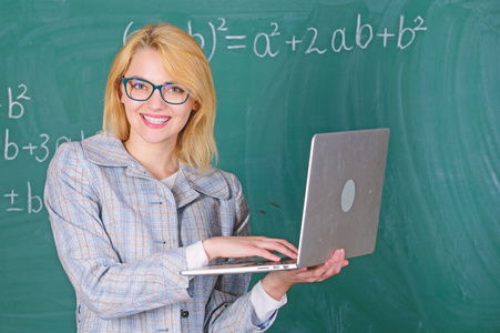 女教师戴眼镜手持笔记本电脑上网。教育家聪明聪明女士用现代笔记本电脑搜索信息黑板背景。用简单的方法学习。数字技术概念