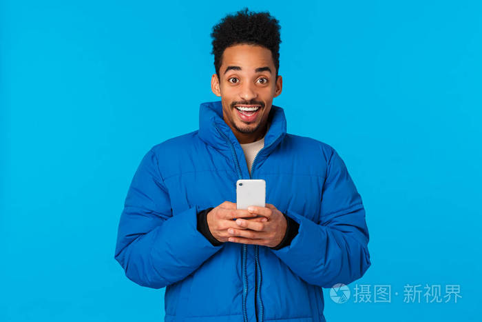 兴奋快乐笑眯眯的非洲裔美国人穿着棉袄拿着智能手机咧嘴笑嘻嘻的接受