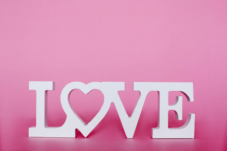 用白色的木制字母书写爱情。爱这个词被放在粉红色的背景上。情人节和妇女节贺卡明信片