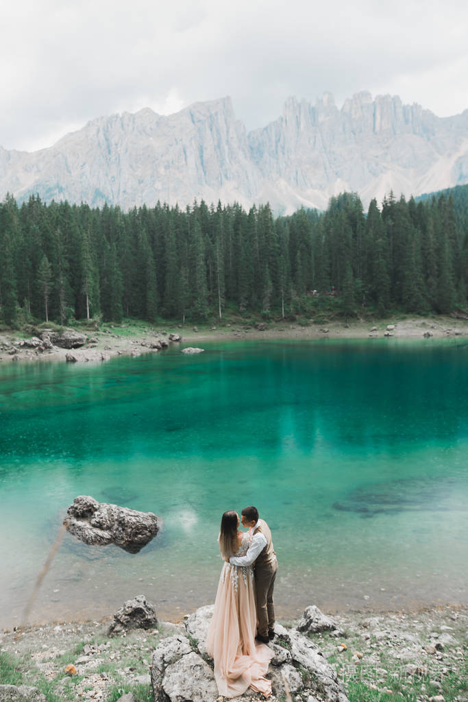 大自然上的新婚夫妇在山中一个美丽的湖边拥抱漂亮的白衣模特儿穿西装