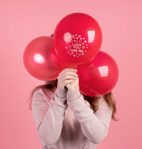 女人用三个红色气球遮住脸，在粉红色的背景上孤立地写着我爱你