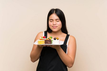 年轻的亚洲女孩拿着许多不同的小蛋糕在孤立的背景下