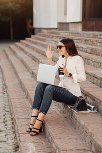 一个穿着牛仔裤和白衬衫的时尚女孩的肖像，拿着笔记本电脑和热咖啡，自由职业者，商务女士，女性权力概念