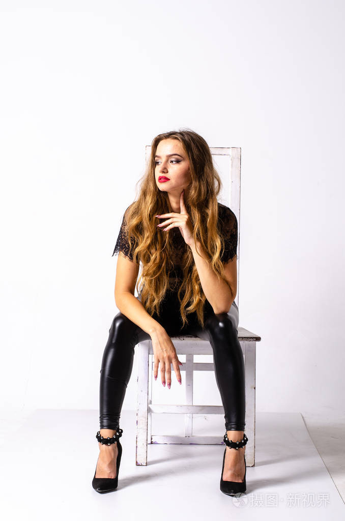 一个黑发女孩的全身肖像穿着皮衣坐着的姿势拿着枪孤立在一个白色的