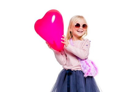 一个穿着粉色毛衣和蓝色裙子的小女孩拿着一个白色背景的红色心形气球