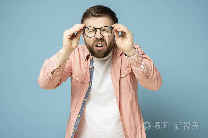 一个视力不佳的白人男子摘下眼镜眯起眼睛透过透明镜片看