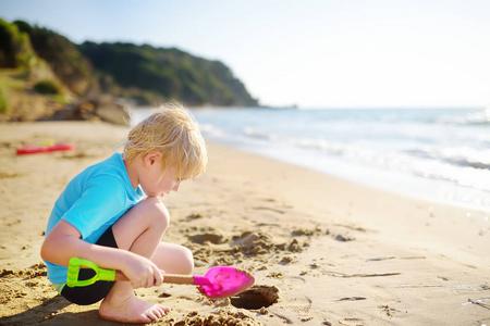 小男孩在希腊海边的沙滩上玩铲子