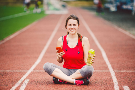 美丽的健身女孩在运动后在体育场使用智能手机.运动和健康.