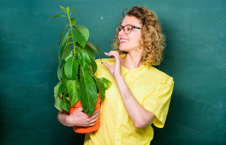 照顾花。快乐的女学生和植物在黑板前。生物课上戴眼镜的女教师。知识之树。环境教育。学校性质研究