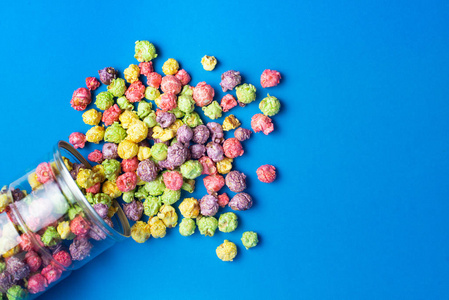 水果味的果仁糖蓝色背景的玻璃杯中的彩色水果味爆米花.糖衣爆米花.