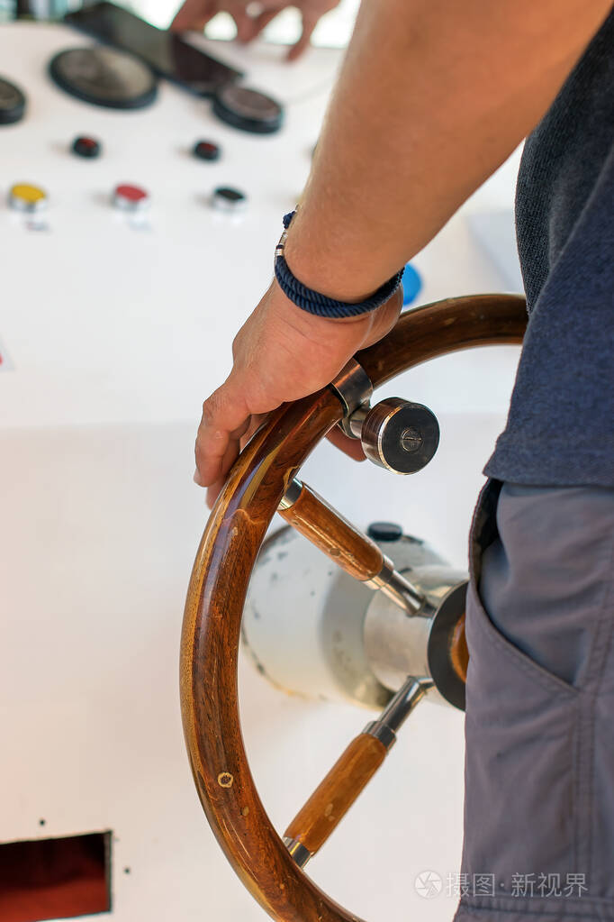 这个人驾驶着一艘海河船一只强壮的男性船长的手放在游艇的舵柄上