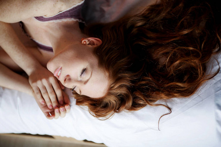 早上在床上，一位年轻迷人的红发女人躺在床上，抱着枕头，微笑着，享受着早晨