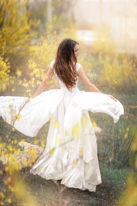 在一个长满了黄花的树木的花园里，一个穿着白色衣服的女人