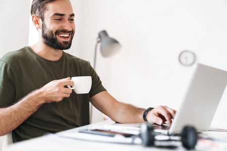 高加索微笑男子在笔记本电脑上打字和喝咖啡的照片