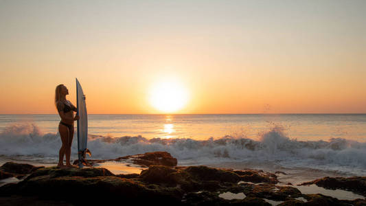 冲浪生活方式。冲浪女孩的剪影与冲浪板在海滩上。金色的日落时间。印度尼西亚巴厘岛