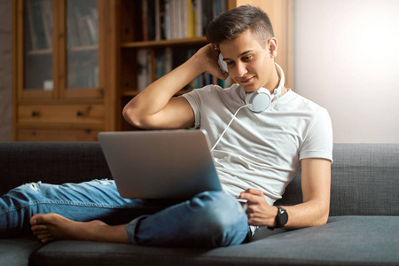 Young handsome man with laptop on gray sofa at home 