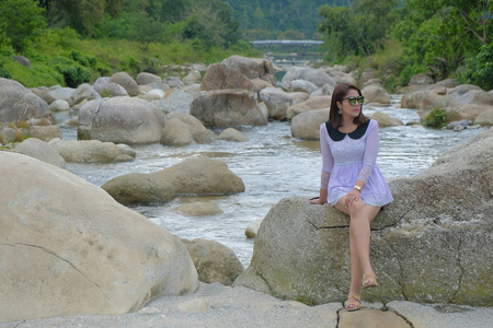 坐在岩石上的亚洲女人背景是一条美丽的水