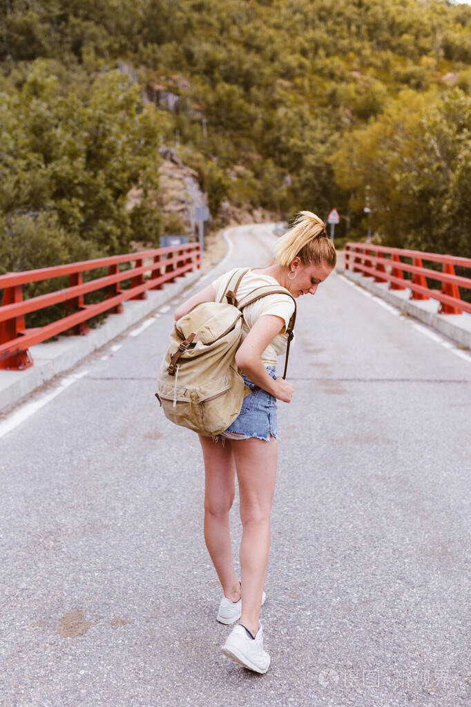 背着背包的年轻金发女人在山附近的一座桥上行走旅行和冒险的概念森林