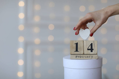 情人节概念。2月14日在木制立方体日历上，白色礼品盒和白色心形在手。白金色背景。
