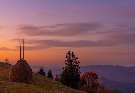 Meadow with haystack and Autumn foliage trees in the mountains 