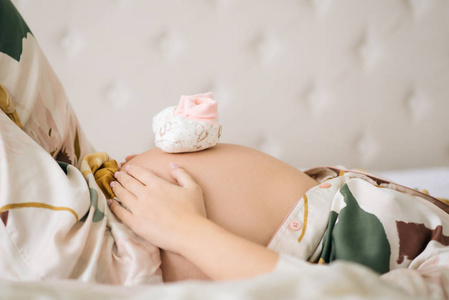 Small shoes for the unborn baby in the belly of pregnant woman. 