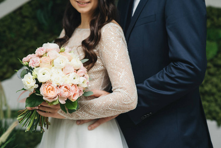 bride holds a wedding bouquet in hands, the groom hugs her from 