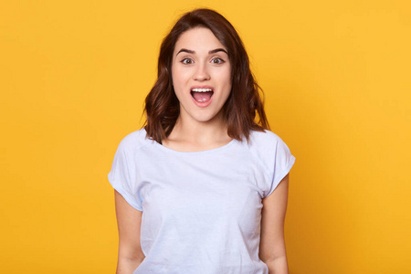 微笑黑发惊讶快乐的年轻黑发女性站在镜头前的特写镜头,表示震惊,张嘴