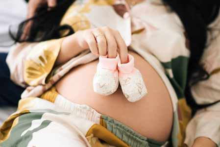 Small shoes for the unborn baby in the belly of pregnant woman. 