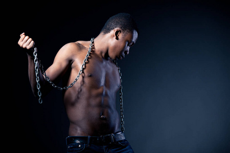 年轻的半裸非洲男子站着，手里拿着巨大的铁链