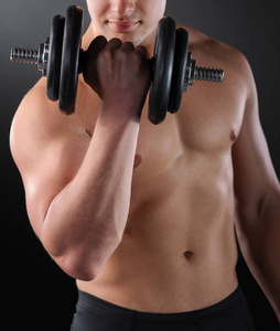 肌肉发达的人在黑暗的背景下用哑铃做练习