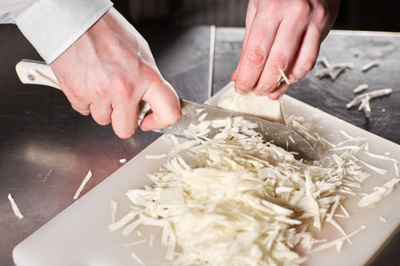 用刀切新鲜蔬菜的手特写.年轻的厨师在白色切菜板上切甜菜.