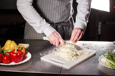 年轻的厨师在白色切菜板上切甜菜.在餐厅厨房做饭照片